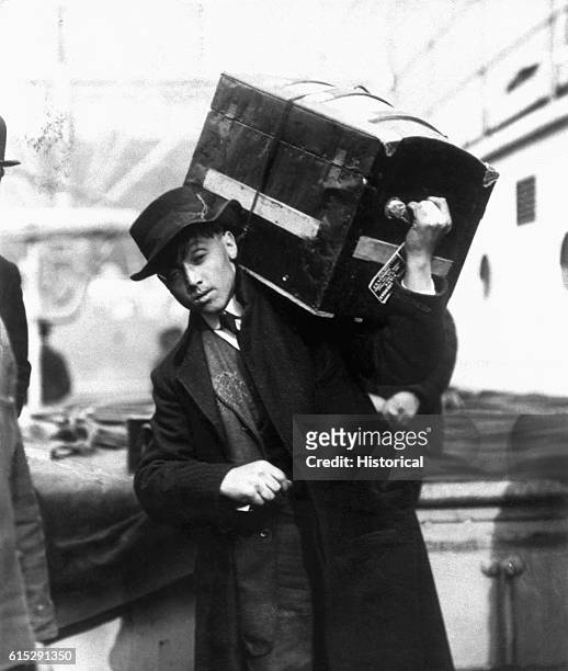 Young Polish immigrant carries a trunk aboard the President Grant at Ellis Island, New York, 1907.