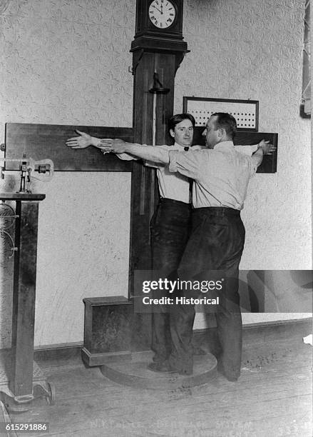 Police officer takes Bertillon measurements of a suspect's[?] arm span at New York Police Headquarters. The Bertillon system is a series of physical...