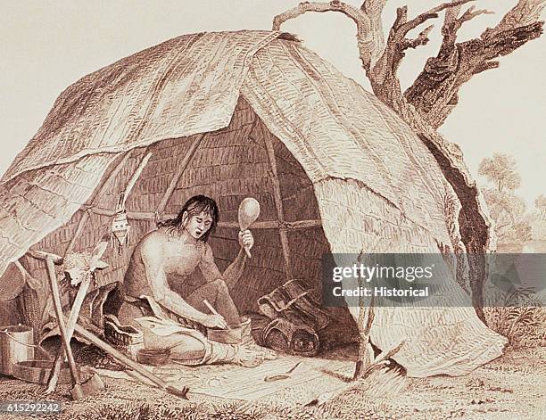 An Native American medicine-man is sitting in a wigwam preparing medicine while holding a gourd rattle and chanting an invocation.