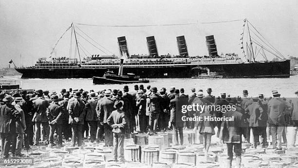Broadside view of the passenger ship Lusitania after her maiden voyage. Viewers watch from a pier. The Lusitania was sunk by a German submarine in...