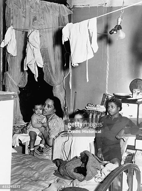 An African American mother and her three children living in poverty in a cramped room. Chicago, Illinois, ca. 1935-1940.