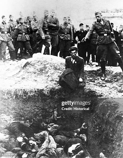 Member of the German S. S. Einsatz Gruppen D prepares to shoot a Polish Jew who is kneeling on the edge of a mass grave almost filled with previous...