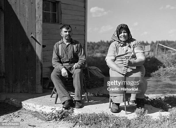 Bohemian farmers of the cut-over land area sit in chairs on a small patio in front of their house. | Location: Black River Falls, Wisconsin, USA,...