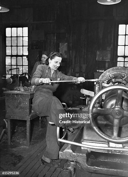 Woman braces with her foot to operate an axle lathe at a car wheel manufacturer in Buffalo, New York. The company began employing women for the war...