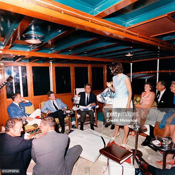 John F. Kennedy opens gifts during a birthday party aboard the Sequoia near Washington, D.C. Among the party are wife Jackie Kennedy and brother...