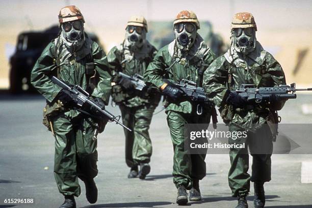 Dressed in chemical warfare suits, gloves and M-17A1 protective masks, four soldiers from the US 82nd Airborne Division walk around their camp to...