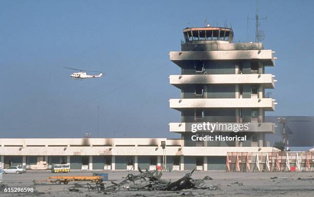 Iroquois helicopter flies by the battle-damaged control tower at Kuwait International Airport while patrolling the skies after the retreat of Iraqi...