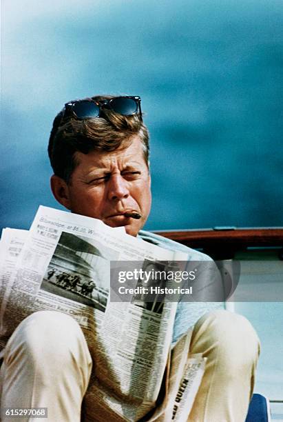 President John F. Kennedy relaxes with a cigar and a newspaper aboard his family yacht, the Honey Fitz. Sailing was one of Kennedy's favorite...