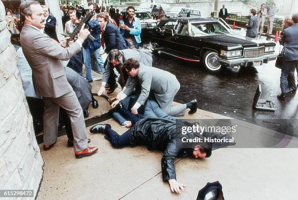 View of armed Secret Service agents around the bodies of policeman Thomas K Delahanty and White House Press Secretary James Brady outside the...