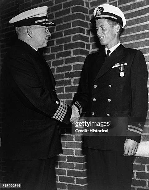 John F. Kennedy shakes hands with Captain Conklin, Commandant, Chelsea Naval Hospital, Boston, after being presented with a medal for heroism in...