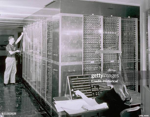 Man closes a clear case door over a section of a large computer while a young woman uses an instrument panel at Los Alamos National Laboratory in New...