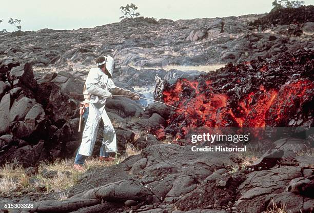 Tilling takes a sample of molten "Aa" lava from a flow on Mauna Ulu. He is wearing special clothing to protect him from the heat. | Location: Kilauea...