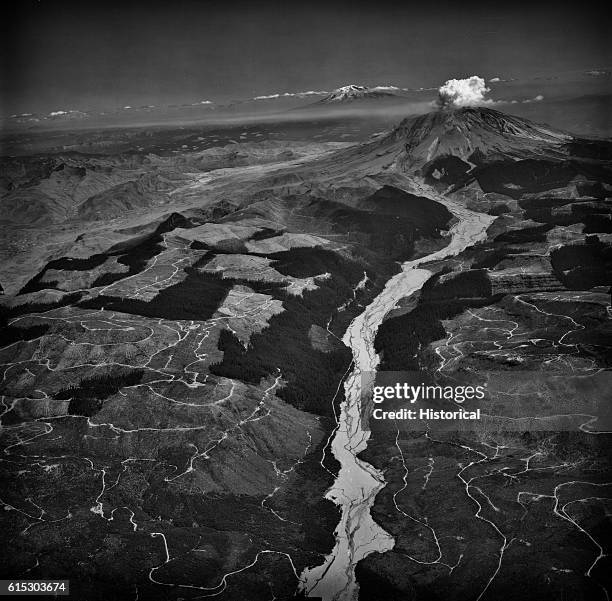 Ash clouds still billow from Mount Saint Helens well over a month after its May 18, 1980 eruption. In the foreground, the ash-clogged Toutle River...