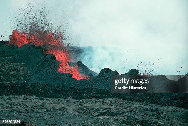 Lava from a bubbling fountain spatters into cooling chunks in the air as it hits a wall of cool rock. Hawaii.