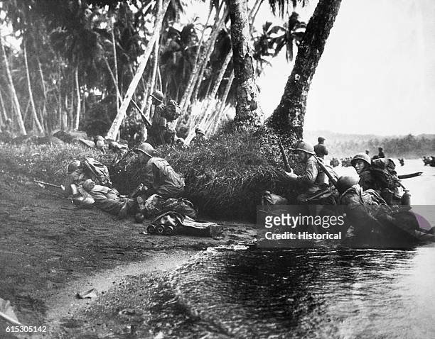 Landing operations on Rendova Island, Solomon Islands. Attacking at the break of day in a heavy rainstorm, the first Americans ashore huddle behind...