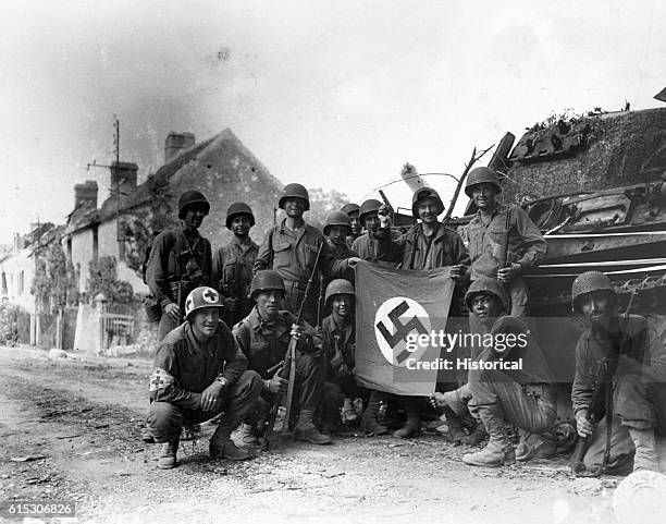 American infantrymen line up in front of a wrecked German tank and display a captured swastika in Chambois, France, the last stronghold of the Nazis...