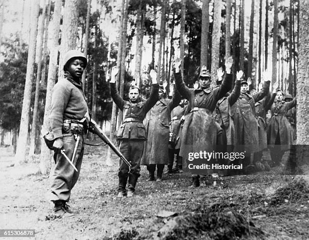 An African-American soldier of the 12th Armored Division stands guard over a group of Nazi prisoners captured in the surrounding German forest. April...
