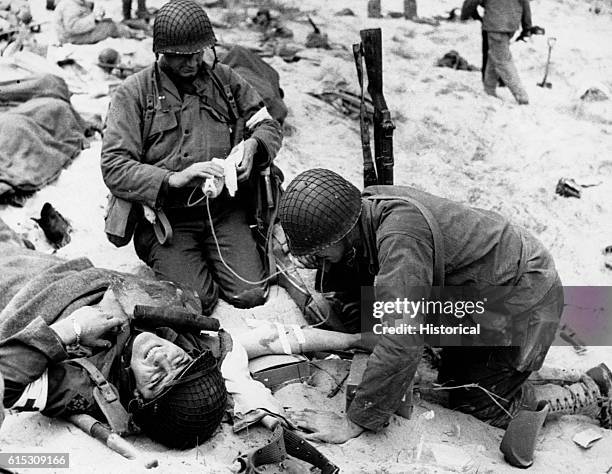 Medics start an IV as they assist a wounded soldier in France after the 1944 Normandy invasion.