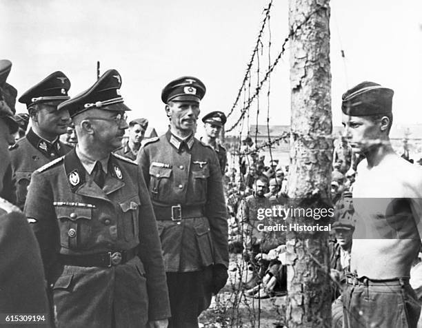 Reichsfuhrer-SS Himmler takes a look through a barbed-wire fence to inspect Russian prisoners of war. Ca. 1940s. | Location: prisoner of war camp.