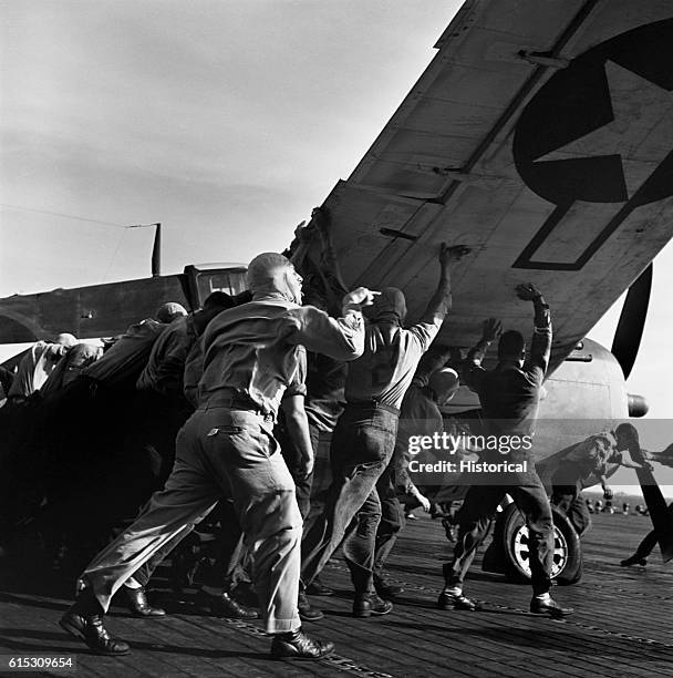 Ens. V. A. Prather directs the deck crew of the USS Lexington as they move a damaged plane out of the way. December 1943. | Location: USS Lexington.