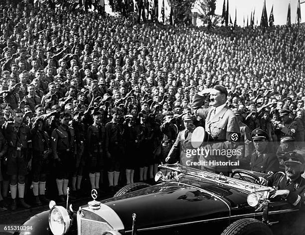 Adolf Hitler salutes a huge crowd of Hitler Youth as he is driven by in a motorcar.