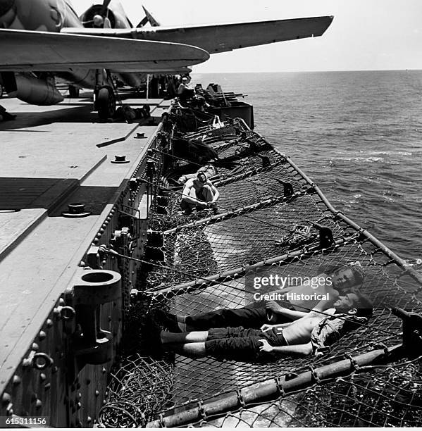 Enlisted men soaking up some Pacific sunshine while lolling in the nets along the flight deck of the USS Saratoga. | Location: on board the USS...