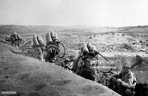 With riflemen leading the way, flame throwing U.S. Marines, bent by the weight of their weapons, move forward toward enemy pillboxes on Iwo Island,...