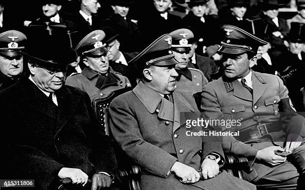 Seated in the audience at a rally or speech are, left to right, Nazi state secretary Remhardt, Reich finance minister Walter Funk, and state...