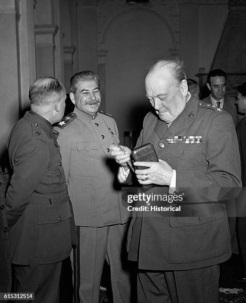 Soviet Premier Josef Stalin and British Prime Minister Winston Churchill stand among other men, talking.