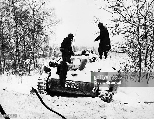 Two soldiers look at a dead crewman on a snow-covered German tank during the Battle of the Bulge. St. Vith, Belgium. | Location: St. Vith, Belgium.
