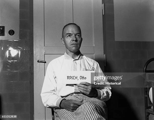 Nazi Otto Rasch, Brigadier General in the SS, member of the SD, and member of the Gestapo, holds his name up on a card. He is on trial in Nurnburg.