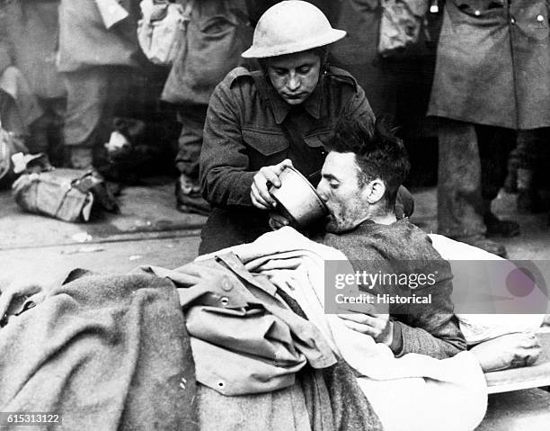 British soldier helps a wounded man drink while waiting to be evacuated from Dunkirk, France in June 1940. British and French troops were forced to...