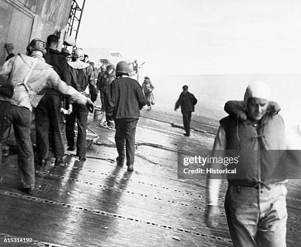 Crew members and fliers examine the damage done the USS Yorktown by the Japanese air raiders in the Battle of Midway. The Yorktown suffered her death...