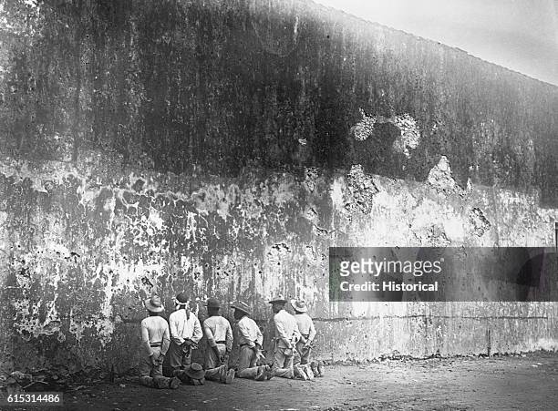 Several Cuban men, kneeling along a wall, await execution by firing squad in Santiago during the Spanish-American War.