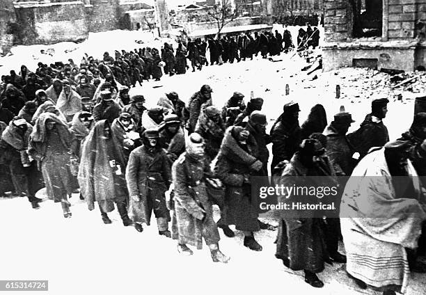 German prisoners wrapped in coats, blankets, or anything they could find to protect against the bitter winter weather, are marched through the snowy...