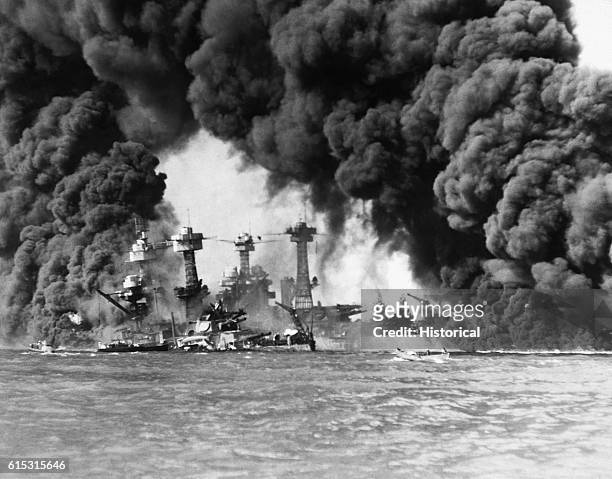 Huge columns of smoke go up from the USS West Virginia and the USS Tennessee, crippled in their berths at Pearl Harbor, Hawaii by a Japanese surprise...
