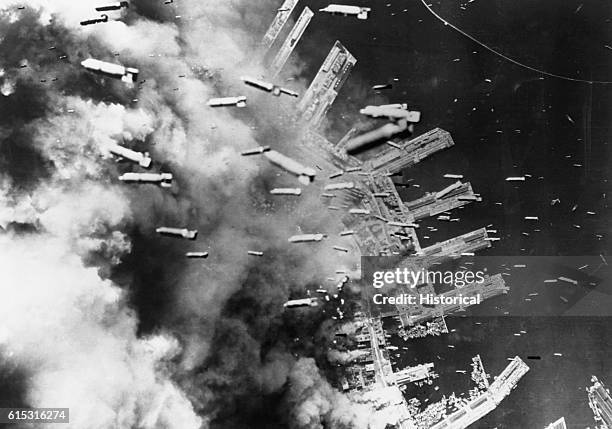 Aerial view of Kobe docks during an air raid using 500 B-29 bombers. Smoke obscures most of the city, with more bombs falling.