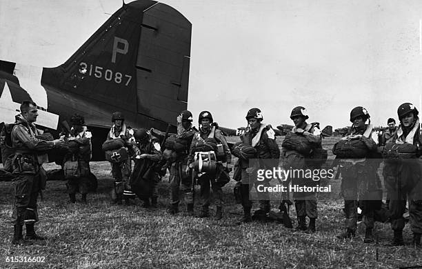 Paratroopers, fully equipped for action, line up on a landing field in England to receive final instructions before boarding a transport plane for...