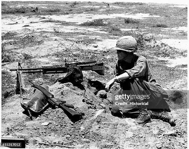 Private First Class John Lakey, with M60 machine gun and M16 rifle, keeps a watch for possible Vietcong as other members of his company "dig in."