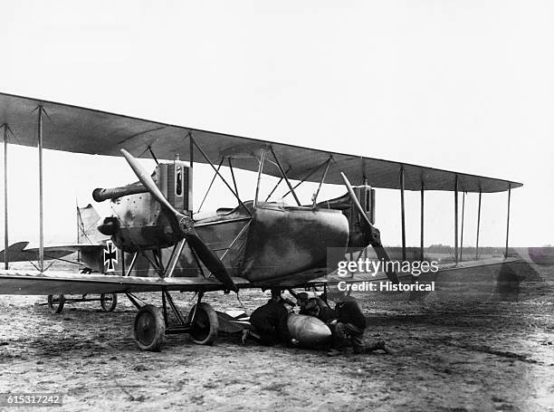 German airmen attach a 100-kilogram bomb to the underside of a Gotha bomber on a bare muddy landing field.