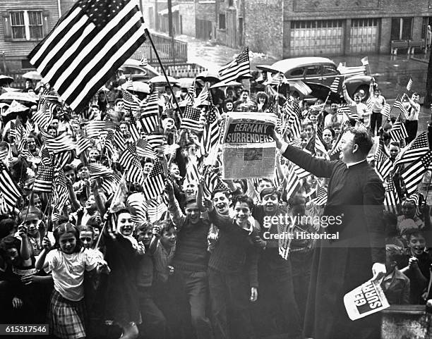 Parish priest waves a newspaper with news of Germany's unconditional surrender to elated pupils of a Roman Catholic parochial school in Chicago.