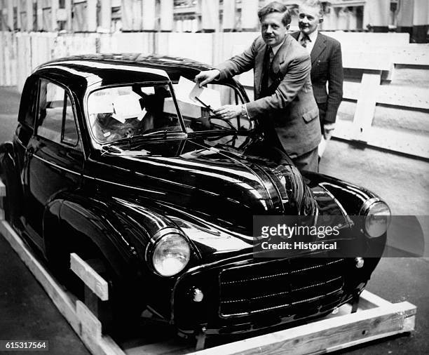 Man plays with the windshield wiper of his Morris Minor automobile.