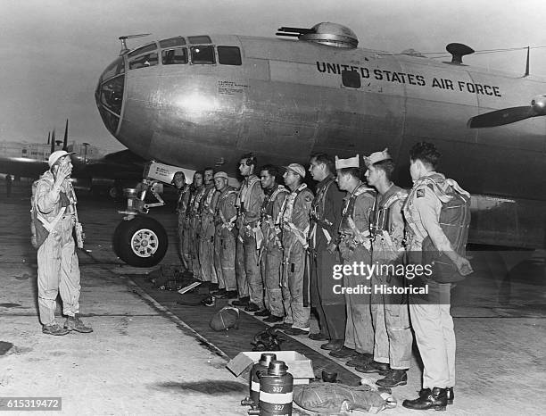 The crew of a B-29 listens to a briefing before a raid on North Korea on an airfield in Japan beside the nose of their bomber.