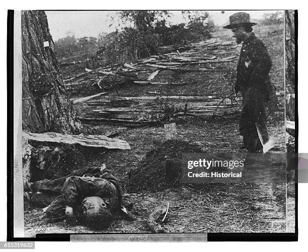 Man stands by the burial mound of a Union soldier. A dead Confederate soldier lies nearby, unburied.