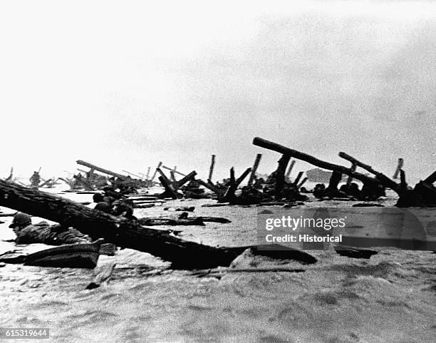 Allied soldiers crawl on their stomachs past log fortifications on Omaha Beach on D-Day, June 6, 1944.