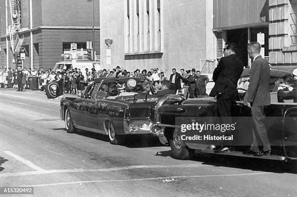 John F. Kennedy's motorcade passes the Texas School Book Depository prior to the assassination on November 22, 1963 in Dallas, Texas.