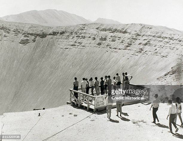 People stand at the edge of a gigantic crater created by the Project Sedan nuclear test explosion. | Location: Near Mercury, Nevada, USA.