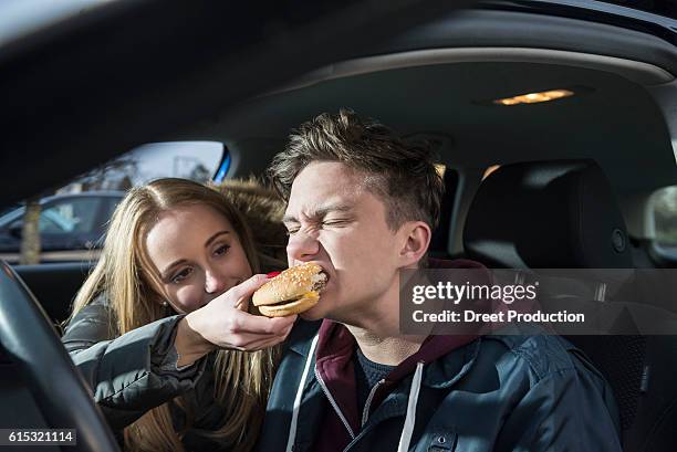 young couple sitting in a car and she is feeding him a burger, munich, bavaria, germany - burger portrait photos et images de collection