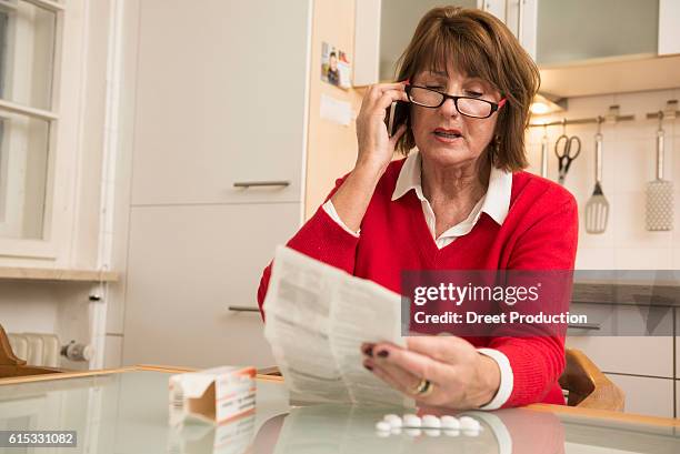 senior woman reading package insert for pills and talking on phone, munich, bavaria, germany - need reading glasses stock pictures, royalty-free photos & images