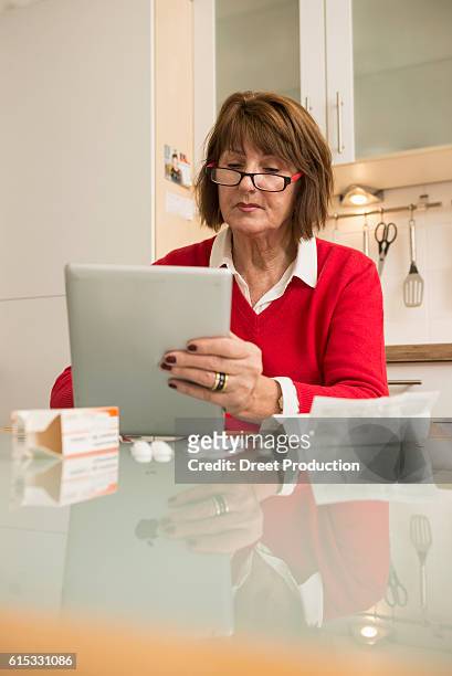 senior woman reading package insert for pills on digital tablet, munich, bavaria, germany - need reading glasses stock pictures, royalty-free photos & images